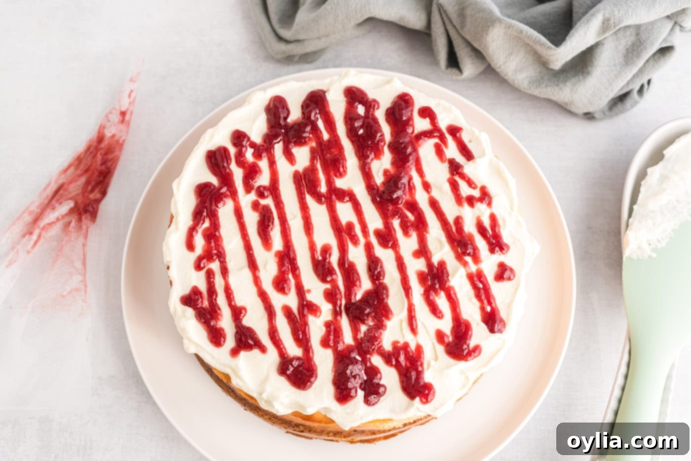 A fine drizzle of warm raspberry preserves being applied from a piping bag onto the whipped cream topping of an English trifle cheesecake.