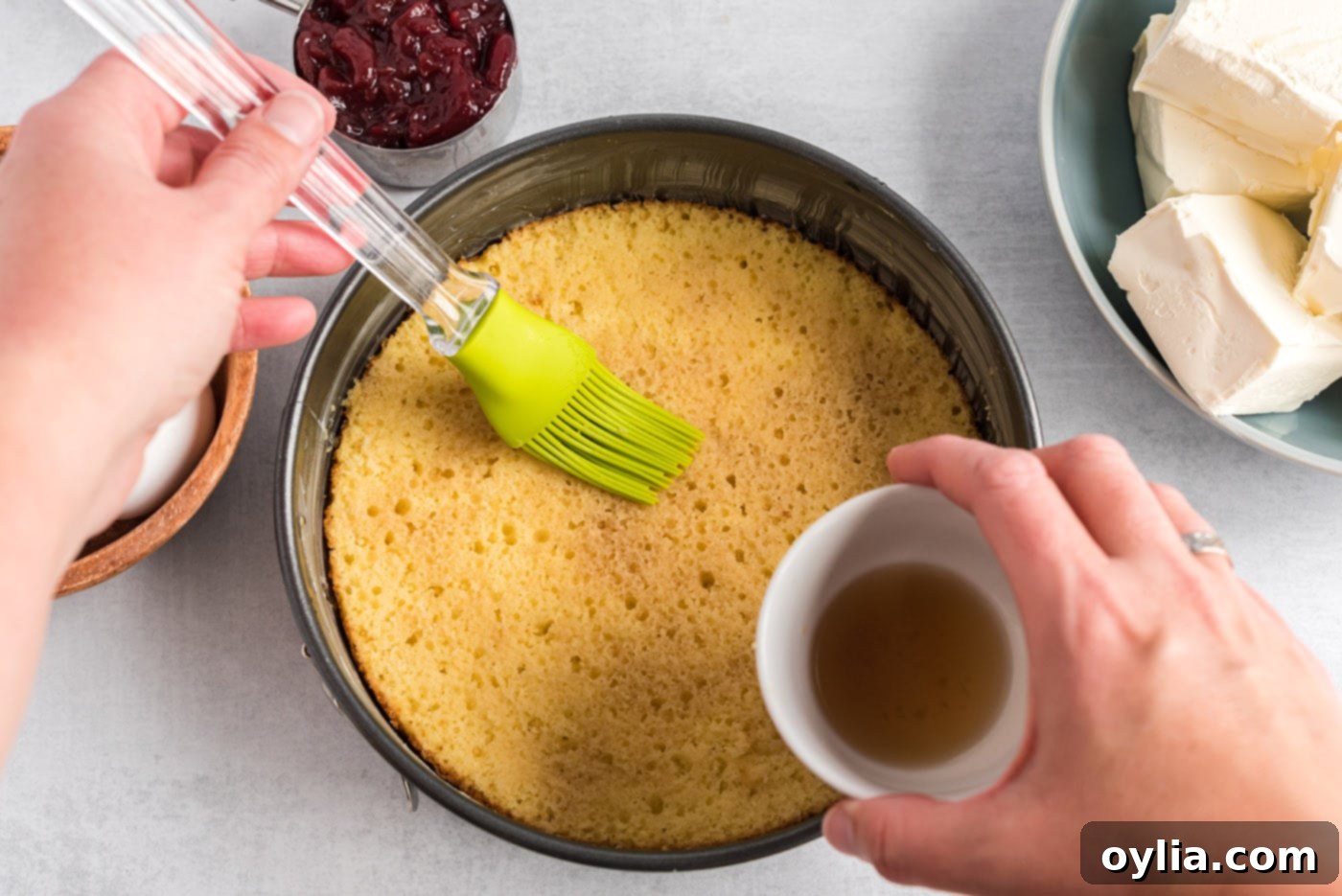 A pastry brush applying sherry to a yellow cake layer in a springform pan.