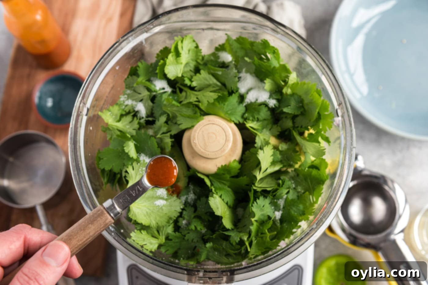 adding hot pepper sauce to food processor with cilantro, onion, avocado, and chile peppers