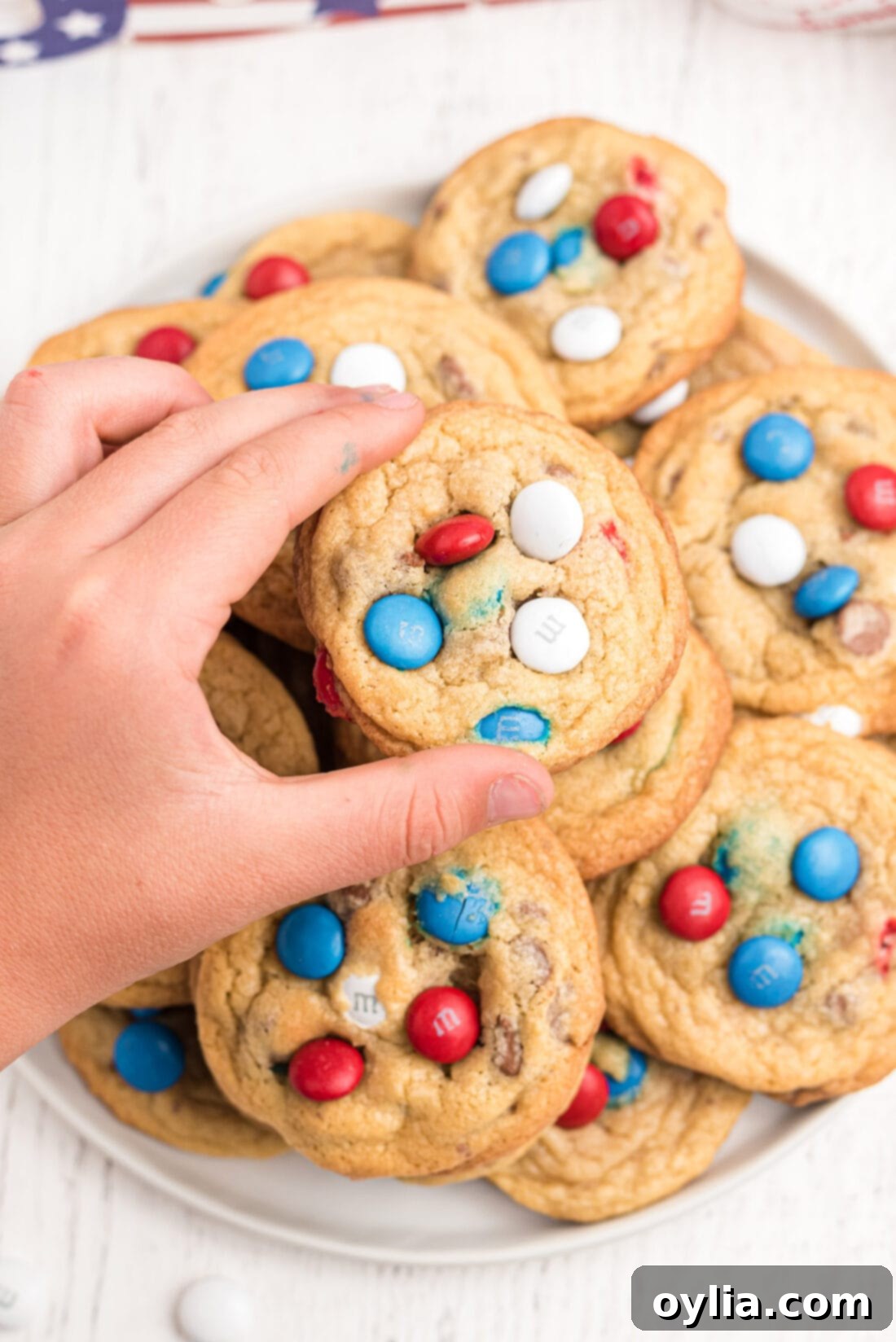 A child reaching for a patriotic red, white, and blue M&M cookie from a plate, perfect for Fourth of July celebrations.