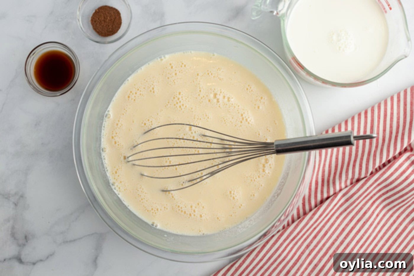 Egg mixture in a bowl with vanilla, nutmeg and milk to the side