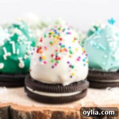 Three Oreo cookies topped with chocolate covered strawberry Christmas trees, adorned with festive sprinkles.