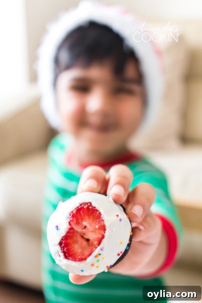 A little boy happily holding out a chocolate-covered strawberry Christmas tree with a bite taken out of it.