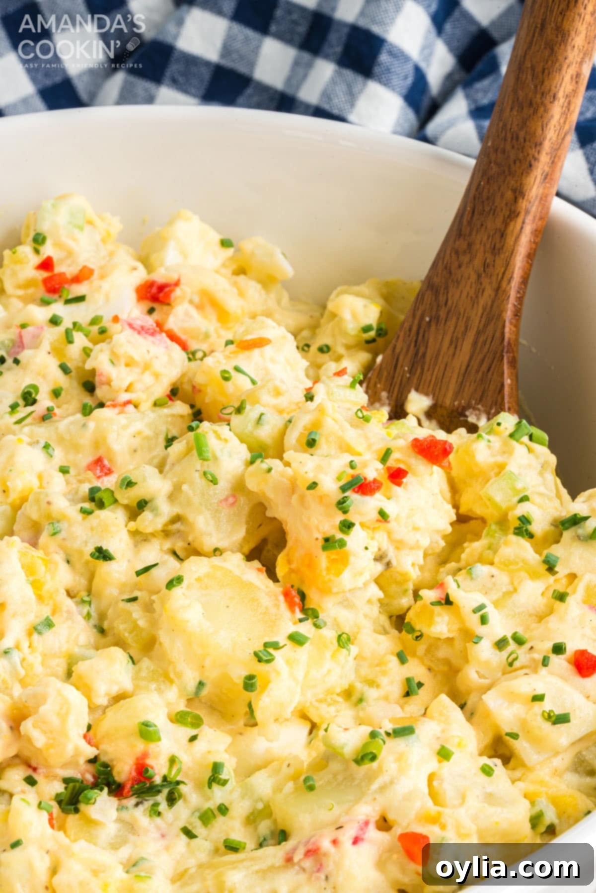 Mom's Famous Potato Salad: A Creamy, Tangy, and Crowd-Pleasing Recipe for Your Next Party! A wooden spoon resting in a large bowl of creamy potato salad, ready to be served at a family gathering.