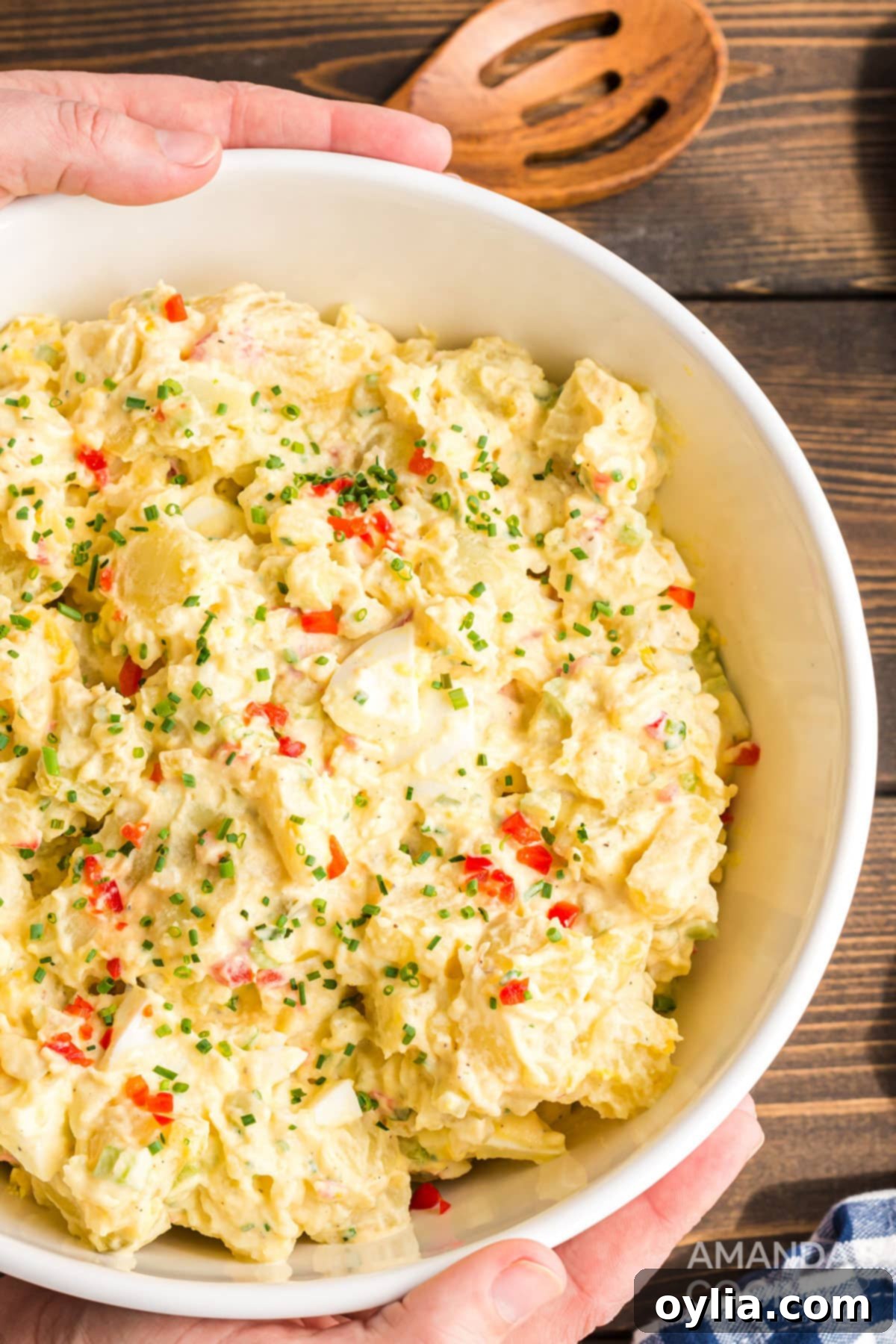 The Ultimate Creamy Potato Salad Recipe: A Family Favorite for Generations. Hands reaching for a large serving bowl filled with a generous portion of freshly made potato salad, signifying its irresistible appeal.