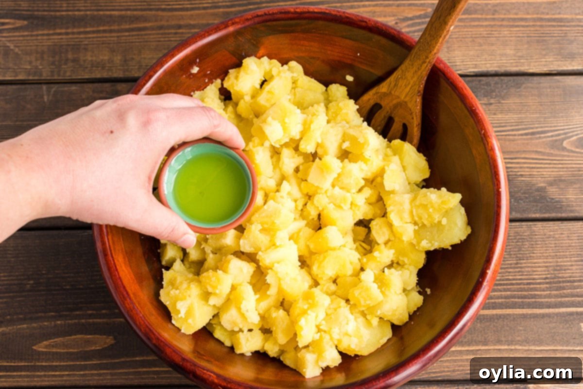 Adding a generous splash of dill pickle juice to a bowl of warm, chopped potatoes, a crucial step for infusing flavor.