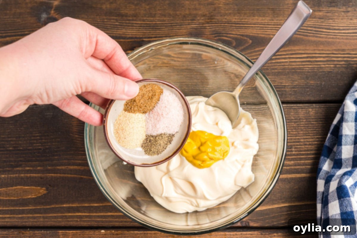 Combining mayonnaise, mustard, and a blend of spices in a bowl, the initial step for creating the creamy potato salad dressing.