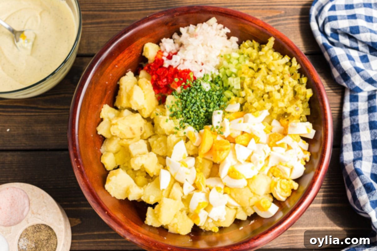 All the freshly chopped ingredients for potato salad, including eggs, celery, bell pepper, onion, pickles, and chives, mixed with the potatoes in a large bowl.
