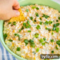 green bowl of corn dip, hand dipping tortilla chip