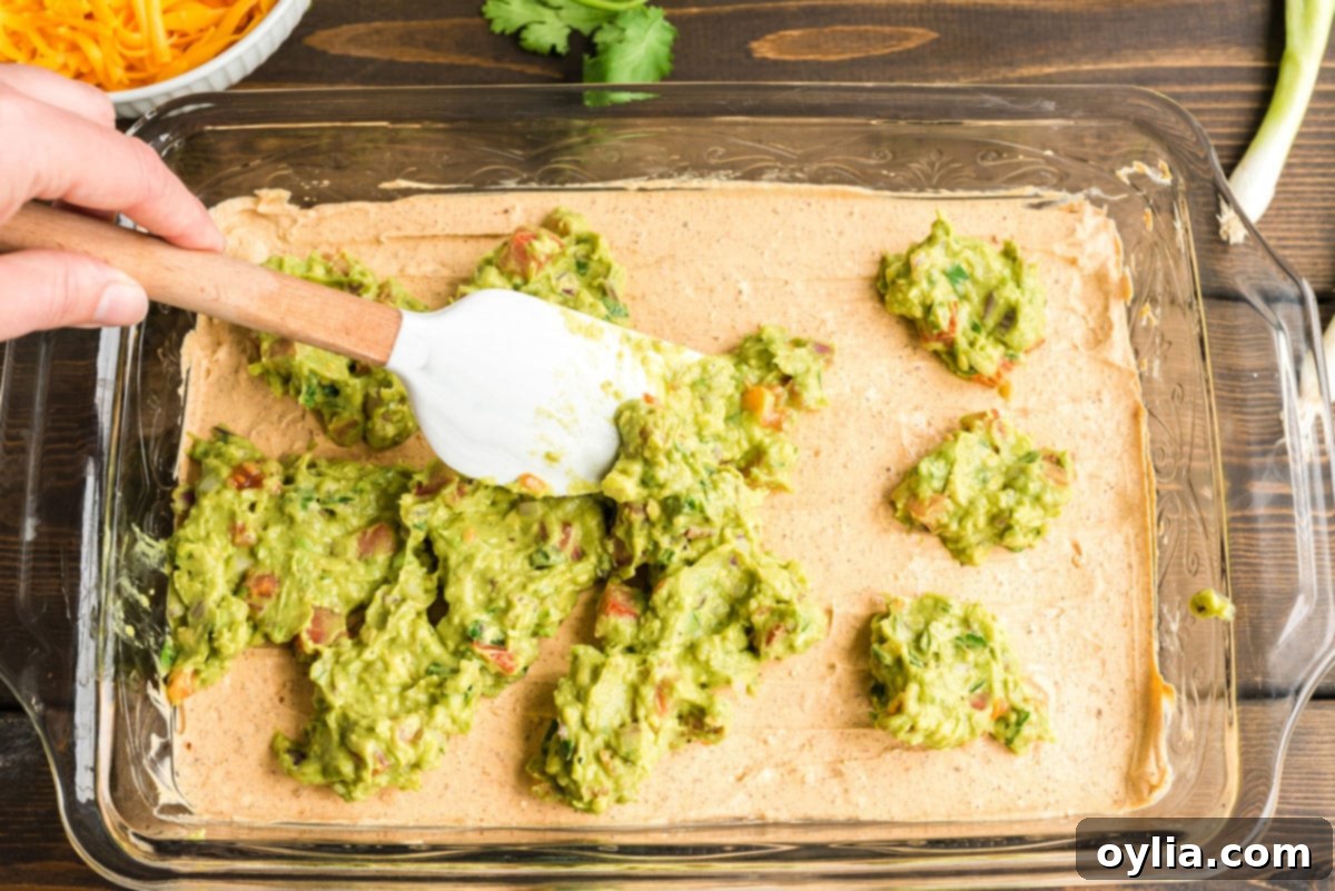 spreading guacamole over sour cream mixture on pan
