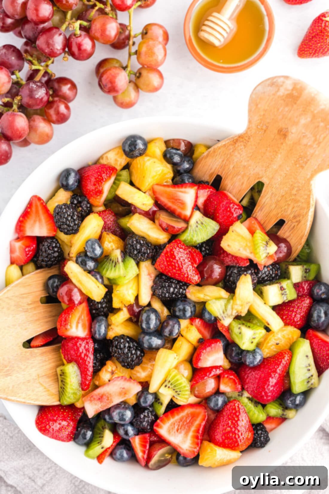 A vibrant bowl of colorful fruit salad with wooden serving spoons, featuring a mix of berries, kiwi, and oranges