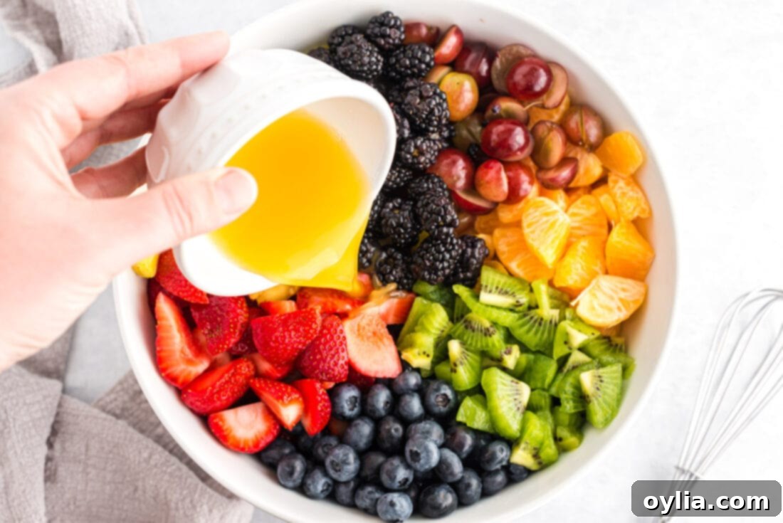 Fresh fruit tossed with the honey-citrus dressing in a large bowl, ready for chilling