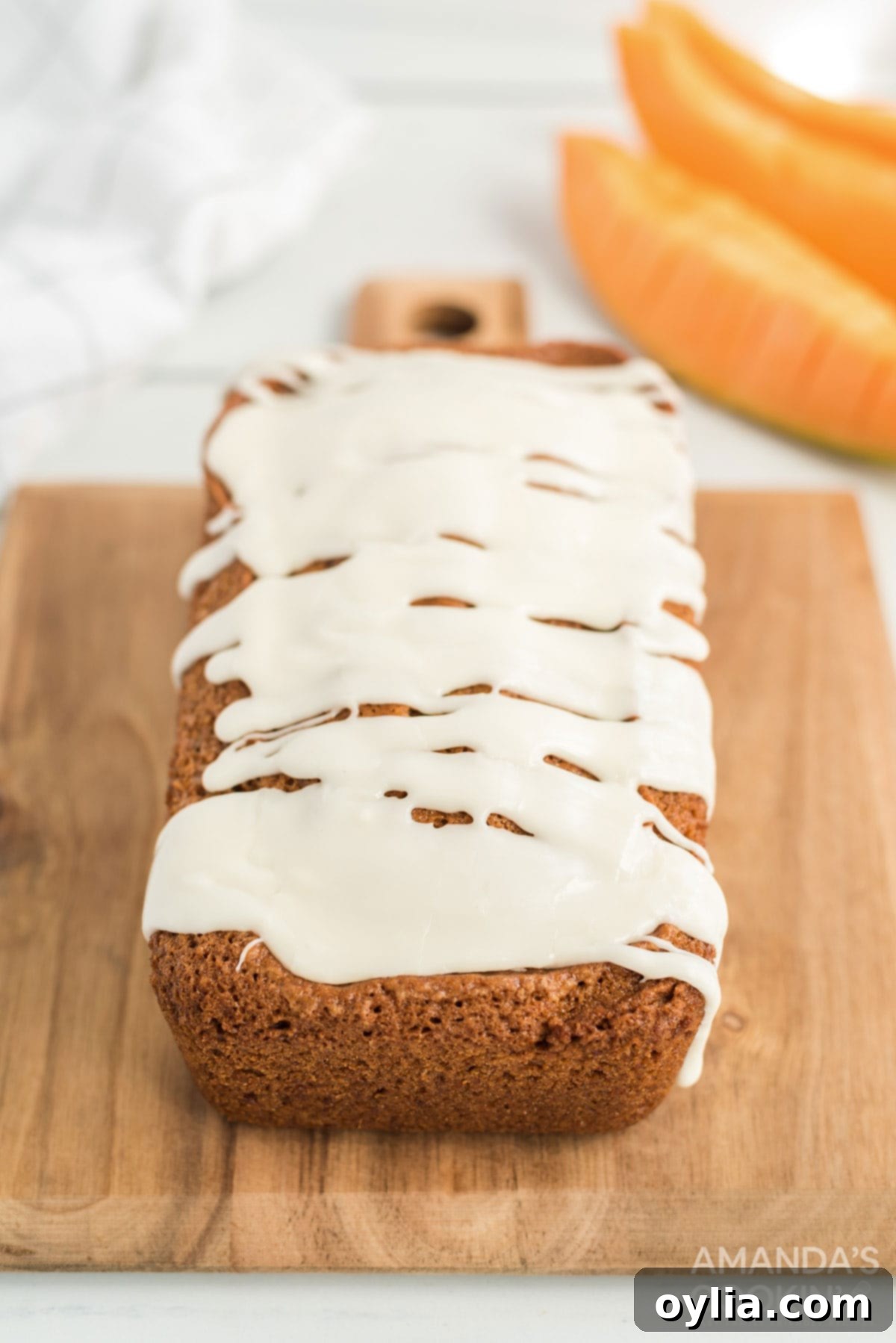 A beautifully iced loaf of cantaloupe quick bread on a wooden cutting board, ready to be sliced.