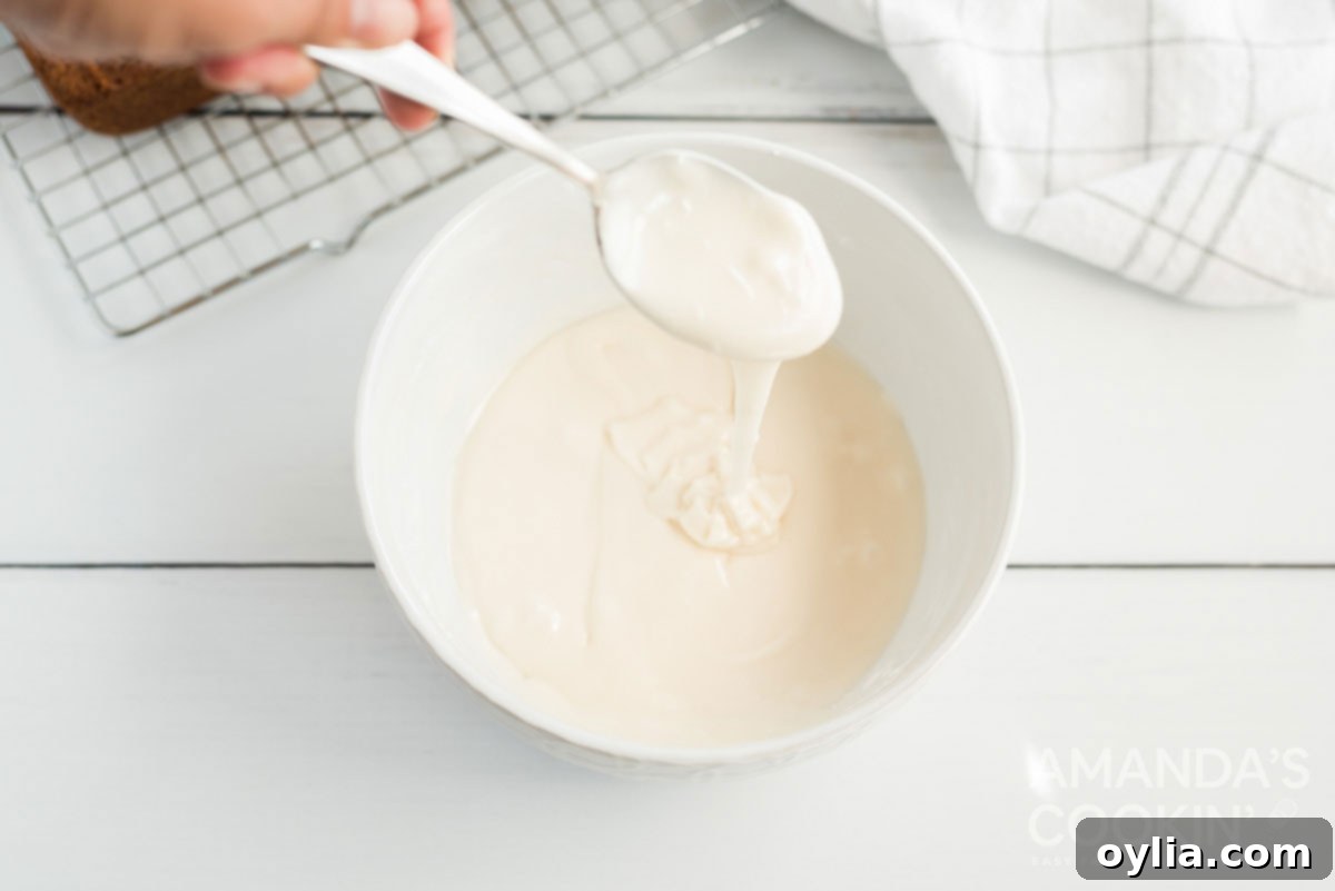 A spoon lifting a stream of thick, creamy powdered sugar glaze, showing its perfect consistency.