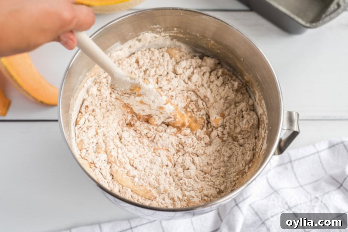 Quick bread batter being gently stirred in a bowl, showing the combination of wet and dry ingredients.