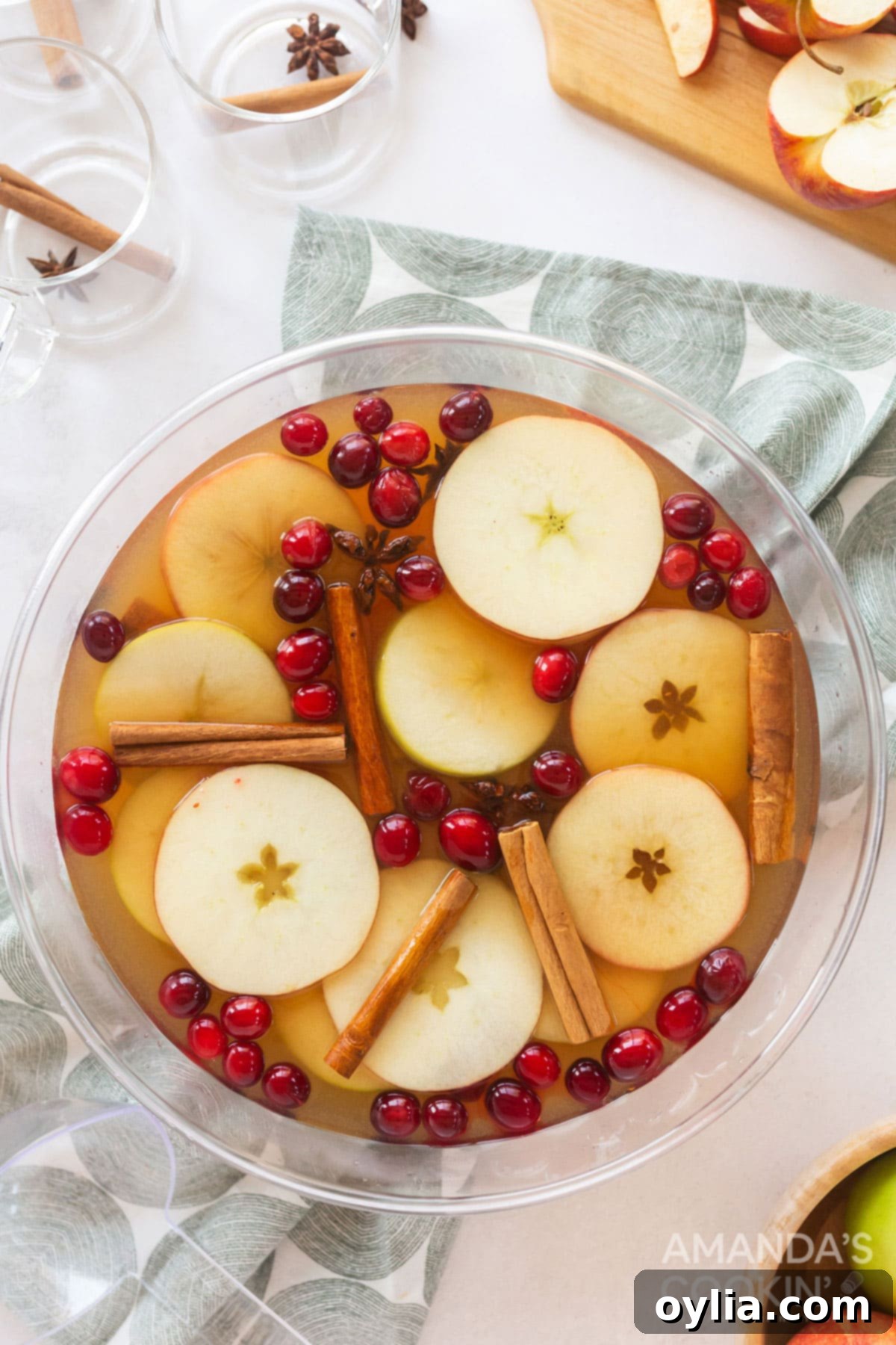 2 simple ingredients plus 2 spicy sweet additions makes this amazing Hot Apple Cider. Think fall festivals, parties, and backyard bonfires! overhead view of a punch bowl filled with hot apple cider and garnished with apple slices