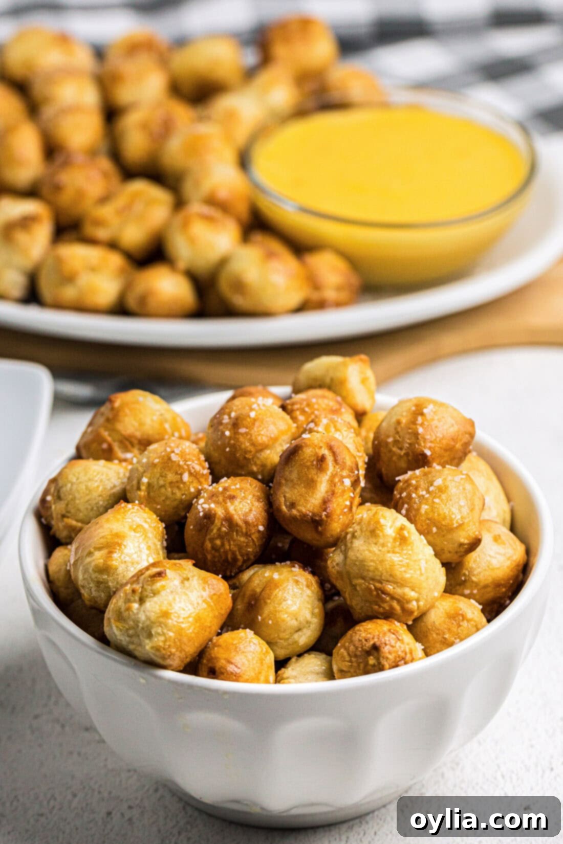 Bowl of Air Fryer Pretzel Bites with more pretzel bites on a platter in the background, ready for dipping.