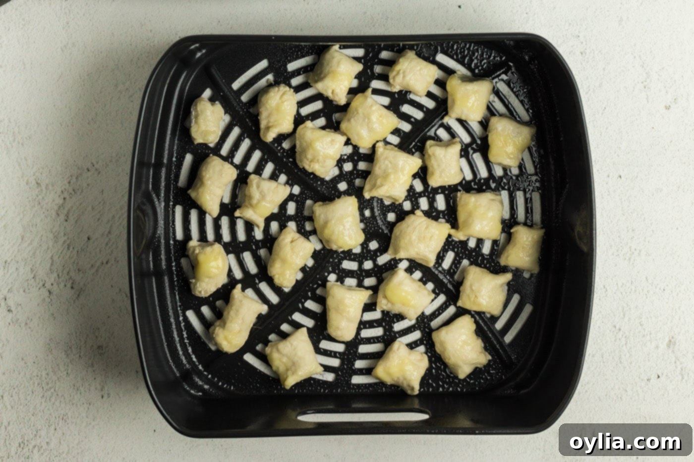 Small pieces of pretzel dough neatly arranged in a single layer within an air fryer basket, ready for cooking.