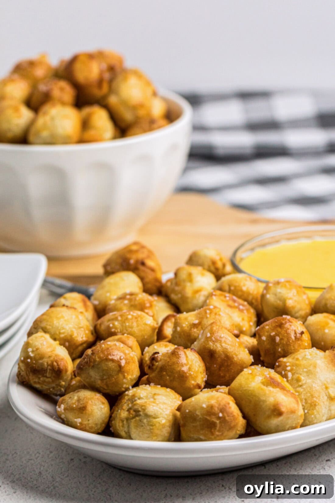 A plate piled high with golden Air Fryer Pretzel Bites, with a bowl of more pretzels in the soft-focus background.