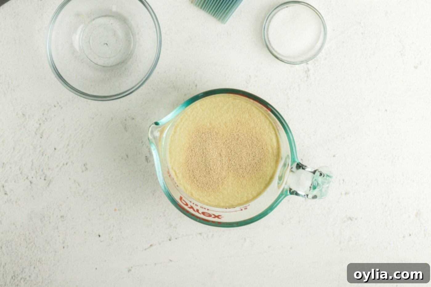 Active dry yeast being added to a liquid measuring cup filled with warm water.