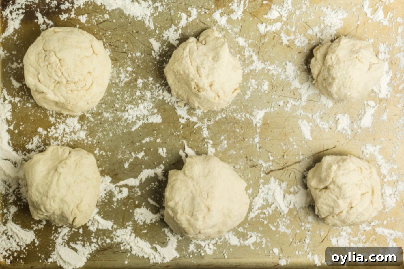 Six evenly divided dough balls on a lightly floured cookie sheet, ready for shaping.