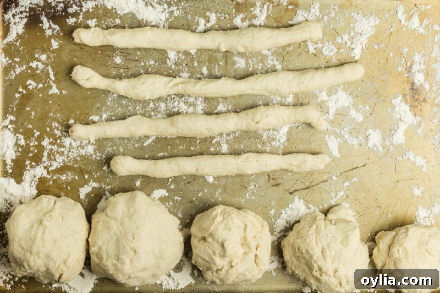 Dough being rolled into ropes on a floured baking sheet, with remaining dough balls ready.