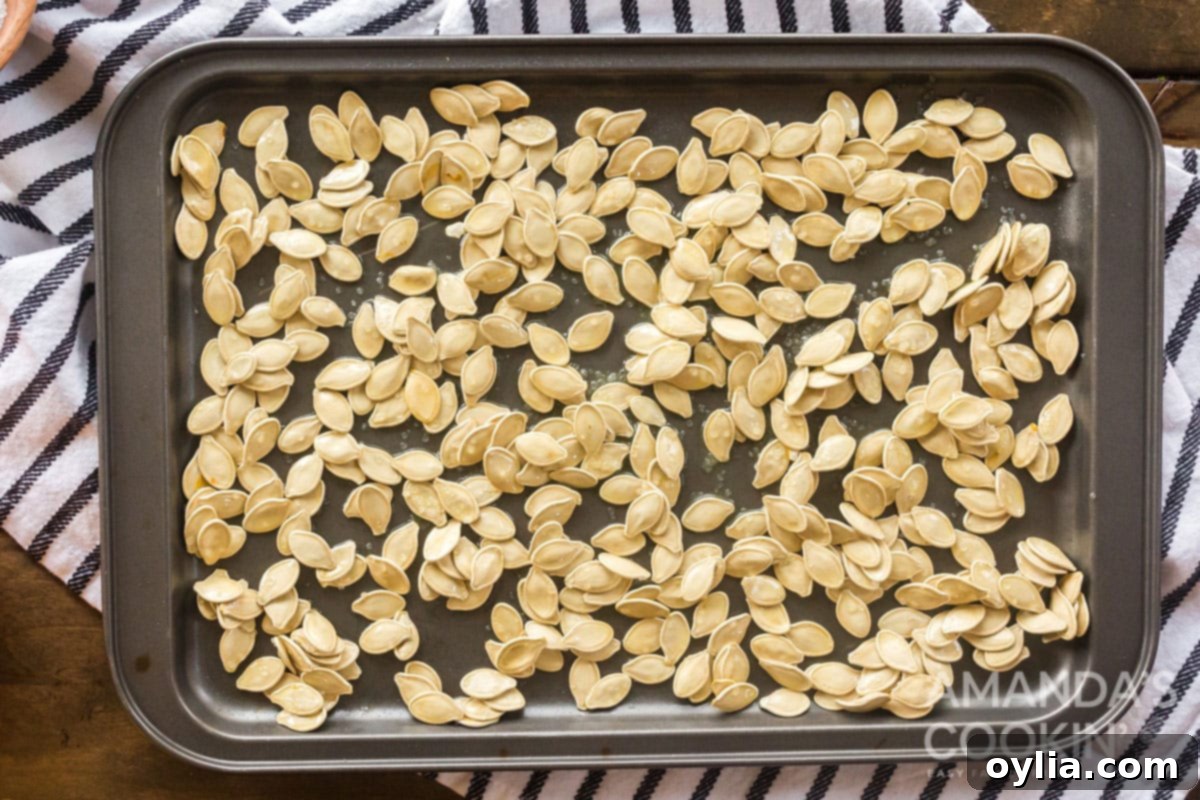 Golden Roasted Pepitas 8 pumpkin seeds seasoned and spread on a baking pan, ready to go into the oven.
