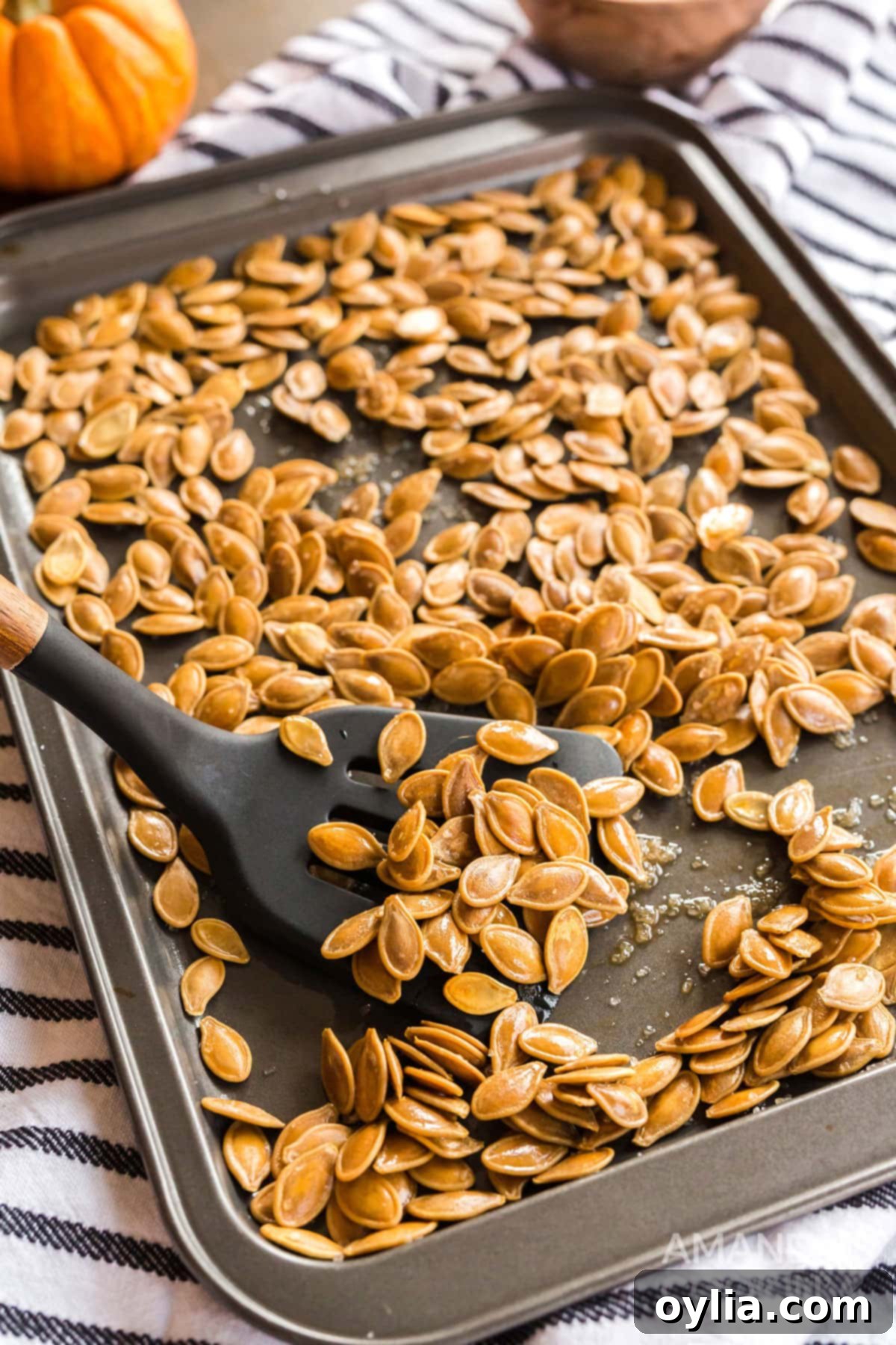 There's something nostalgic about a pan full of salty roasted pumpkin seeds! It's a fall and Halloween tradition after carving pumpkins. cookie sheet of freshly roasted pumpkin seeds with a spatula, ready to be enjoyed as a savory snack.