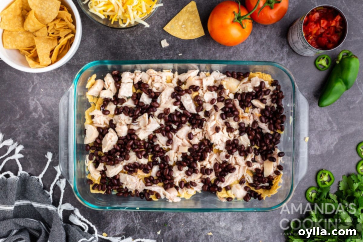 Diced cooked chicken and black beans layered over the crushed tortilla chips in the casserole dish.