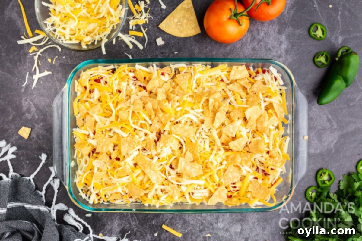 Shredded cheese and the final layer of crushed tortilla chips covering the casserole ingredients.