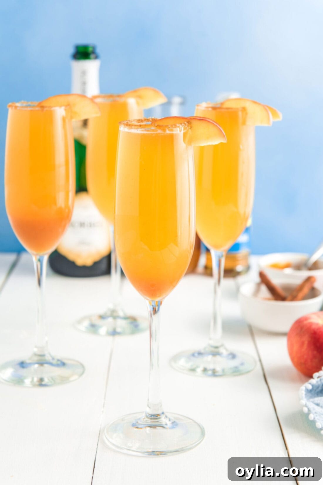 Four glasses of Caramel Apple Mimosas, garnished with apple slices, sitting on a wooden surface.