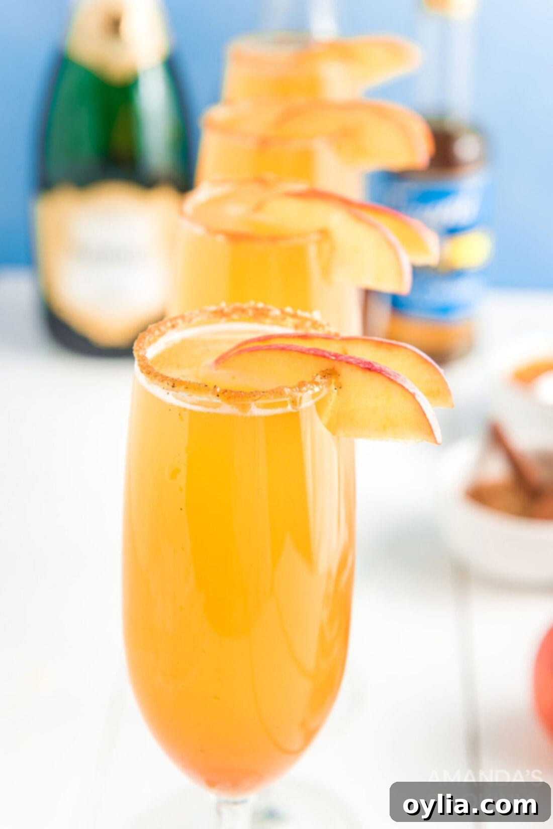 Caramel mimosas garnished with fresh apple slices and a cinnamon stick, beautifully arranged on a dark background.