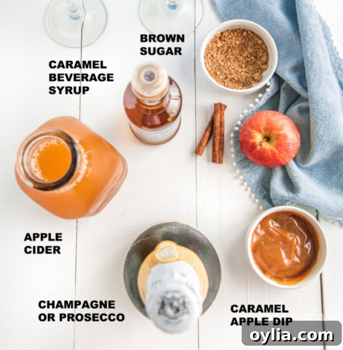 Labeled ingredients for caramel apple mimosas, including brown sugar, cinnamon, caramel dip, champagne, apple cider, and apple slices.