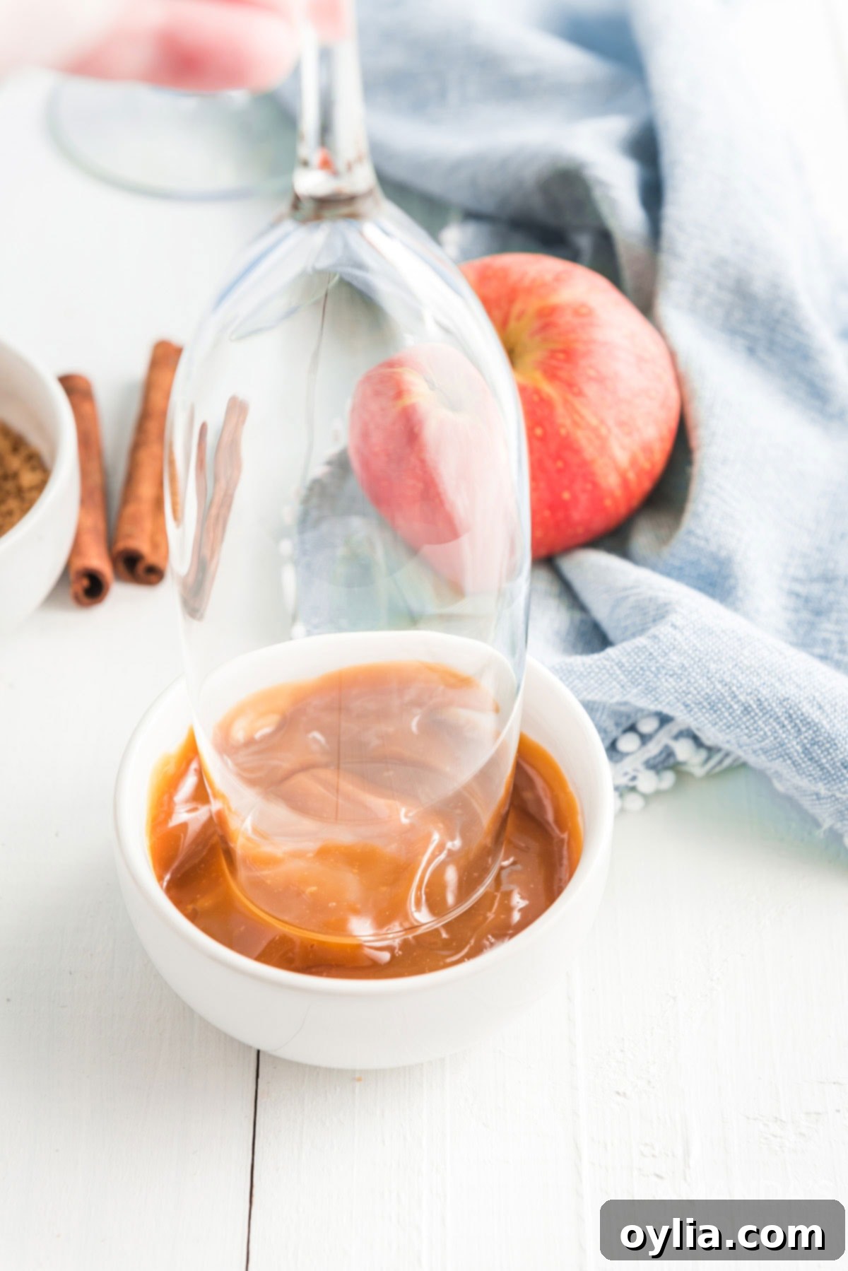Dipping the rim of a champagne glass into caramel dip in a small white bowl.