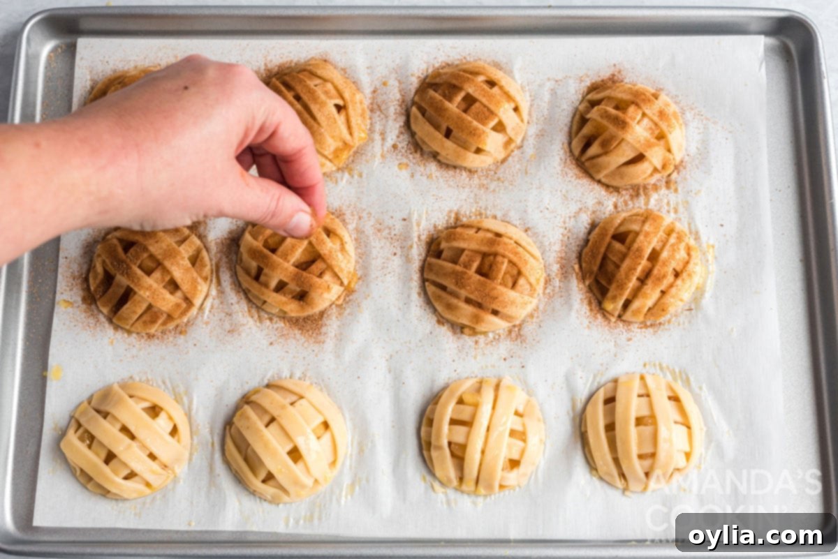 Cinnamon sugar mixture being sprinkled over egg-washed apple pie cookies, ready for baking.