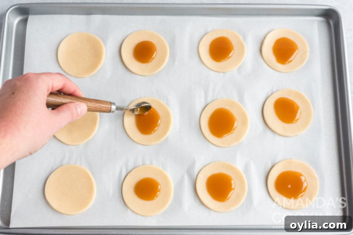 Close-up of small dollops of caramel sauce being added to the center of pie dough circles on a baking sheet.