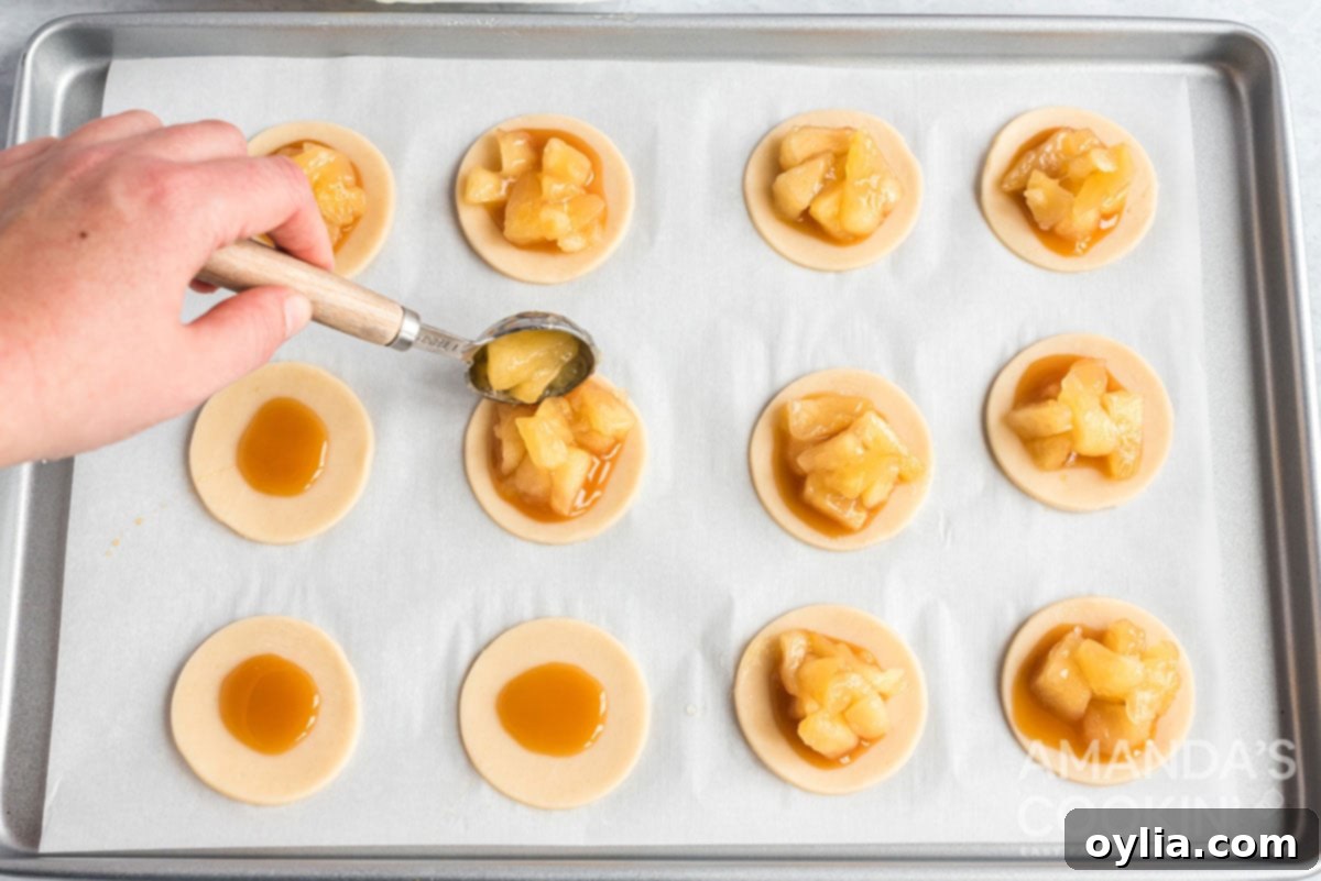 A tablespoon of diced apple chunks being added on top of caramel sauce on a pie dough circle.