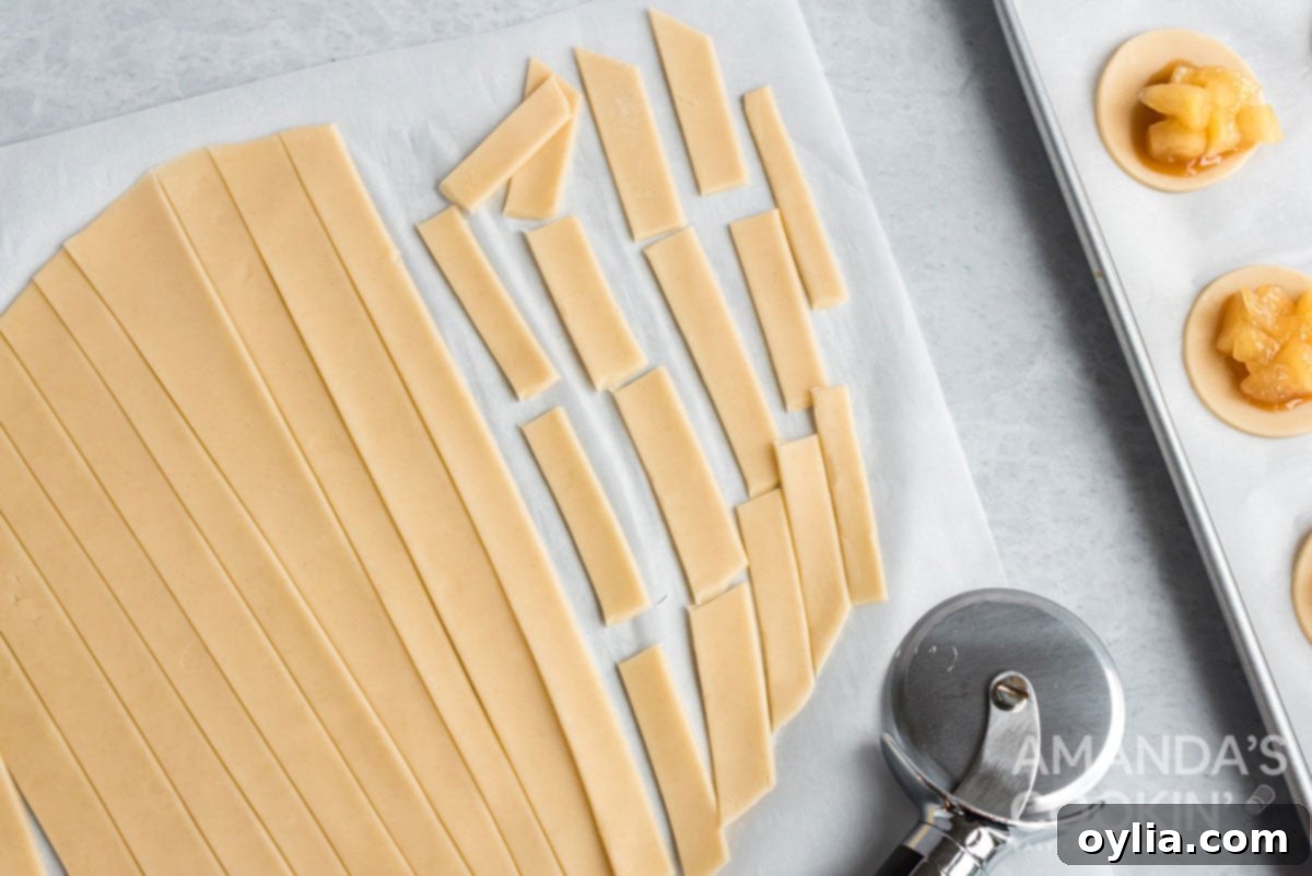 Pie dough being cut into uniform strips using a pizza cutter on a floured surface.