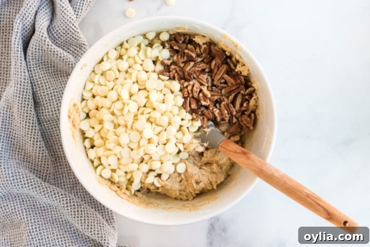 White chocolate chips and chopped pecans in a mixing bowl with cookie dough
