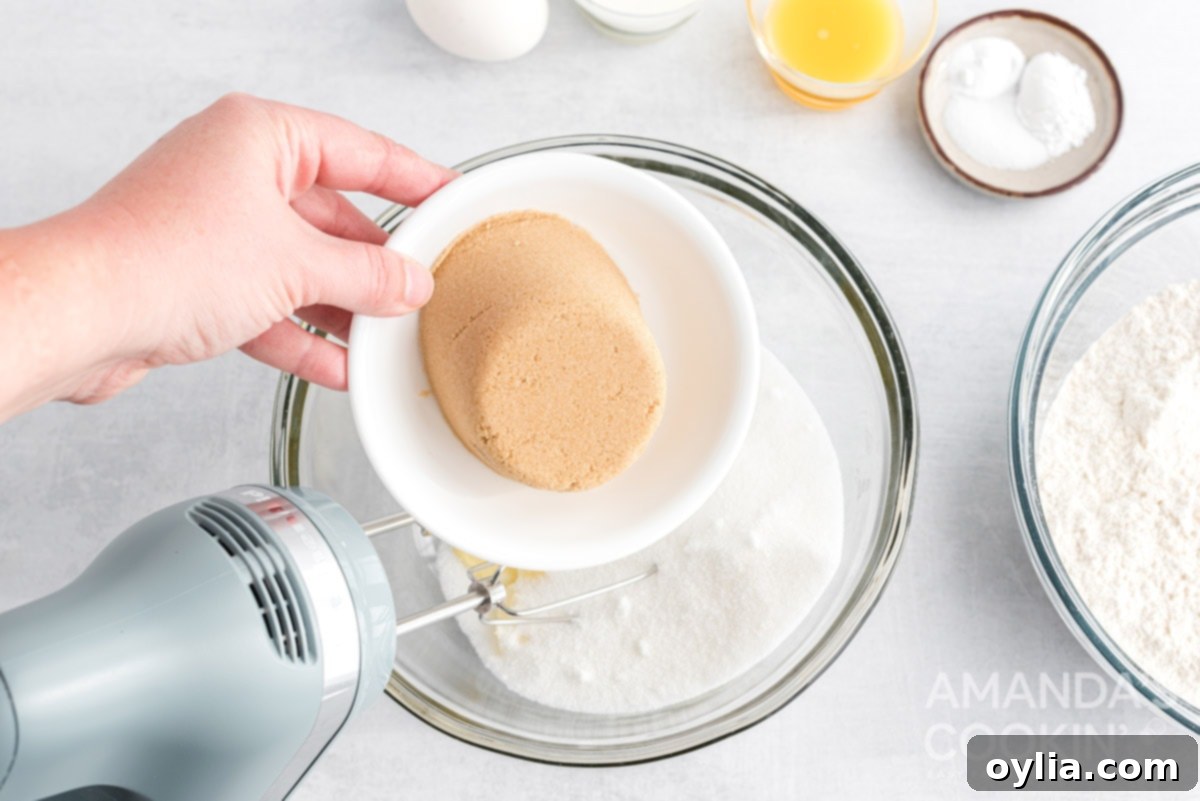 Adding brown sugar to a mixing bowl with creamed butter and granulated sugar