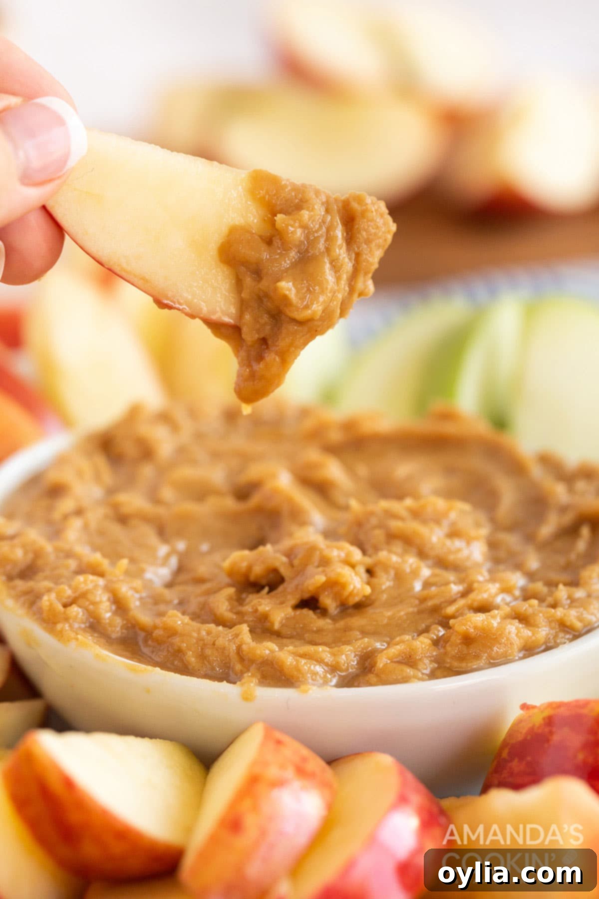someone holding an apple slice covered with peanut butter dip, showing a perfect bite