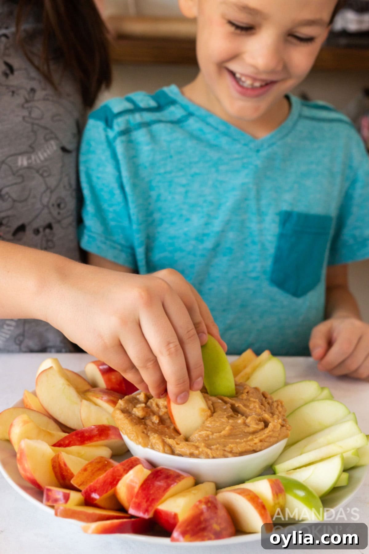 kids happily dipping apple slices into a bowl of peanut butter fruit dip, emphasizing its kid-friendly nature