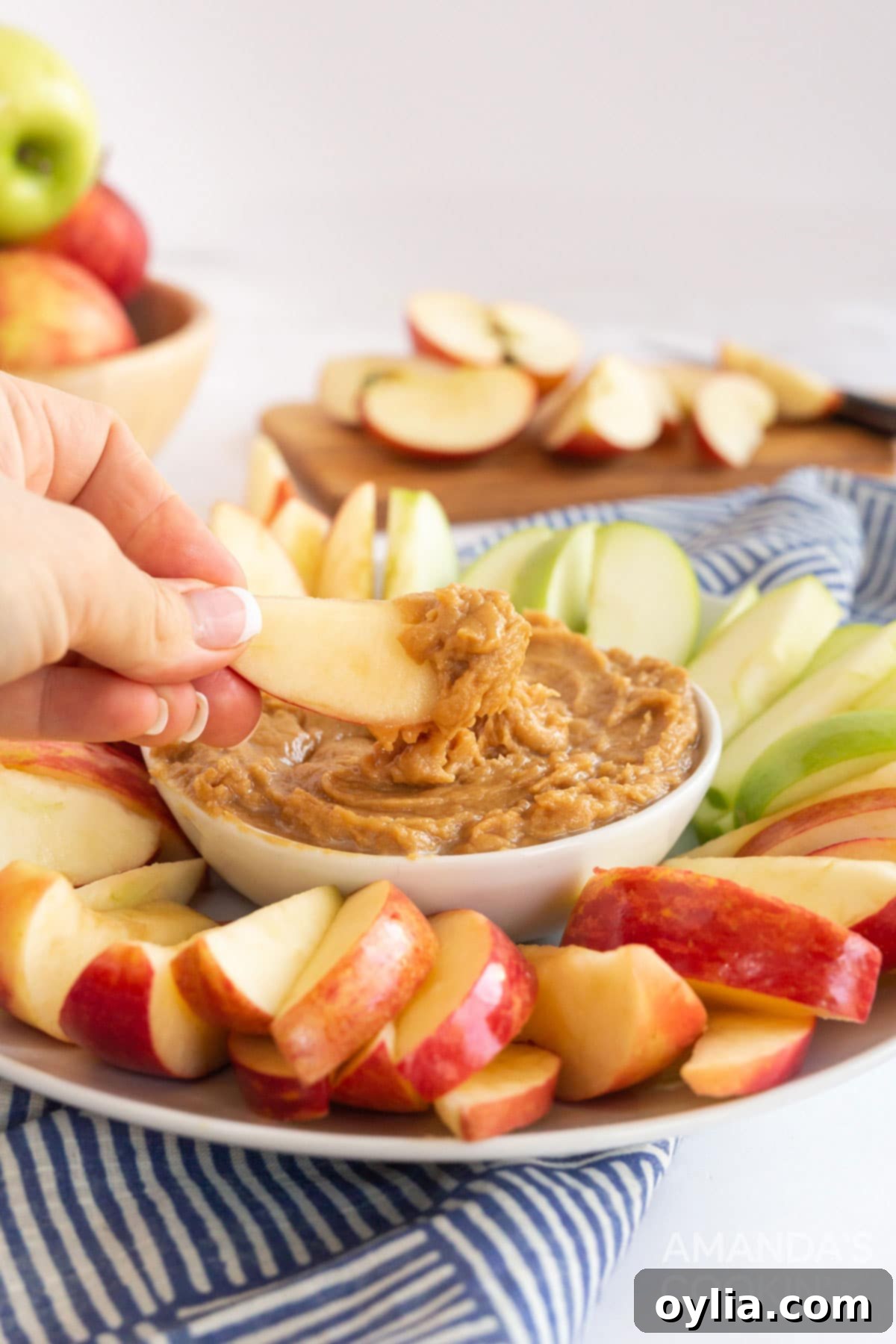person dipping a fresh apple slice into a bowl of creamy peanut butter apple dip, showcasing the simple pleasure