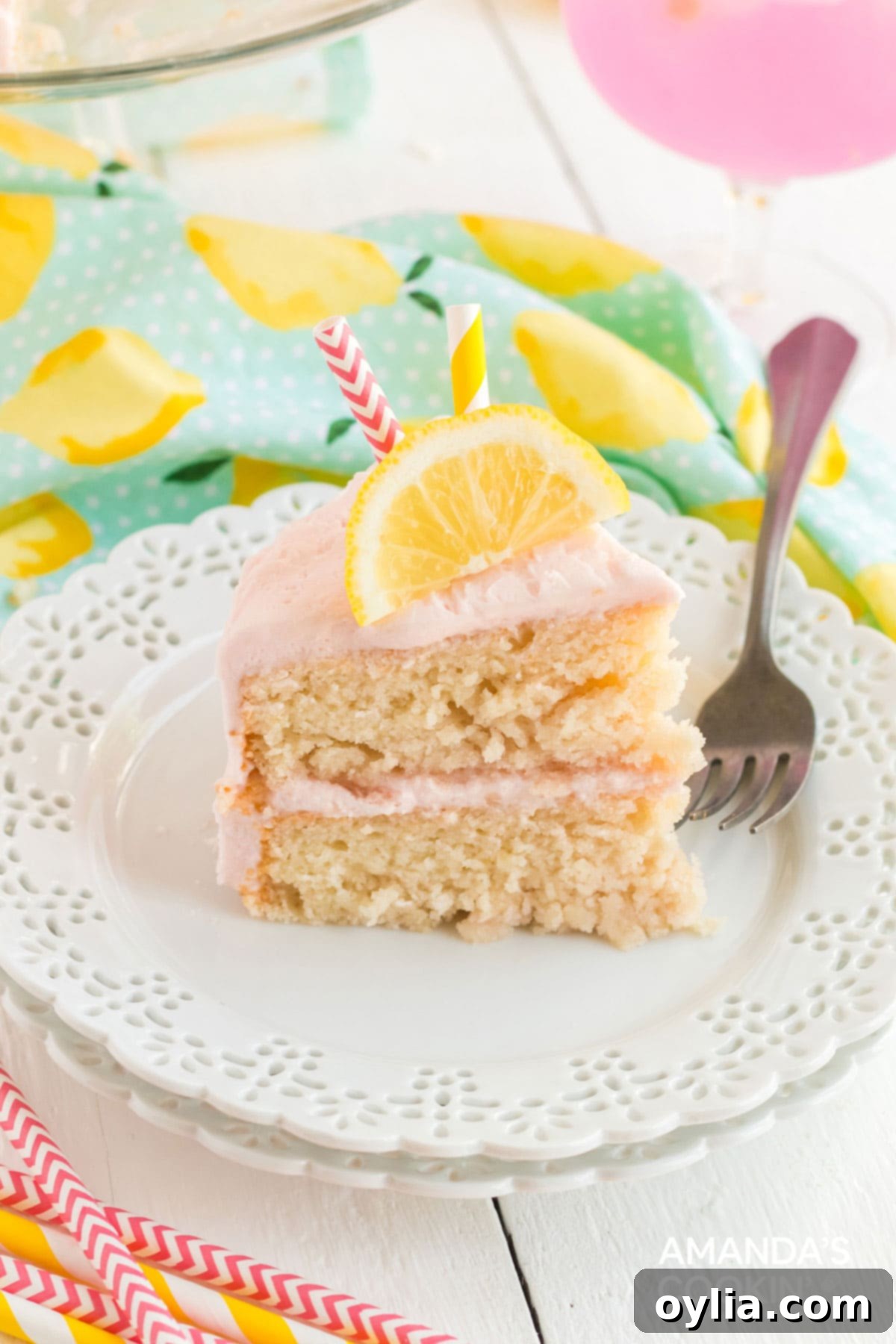 This pink lemonade cake is perfect for summer and will be a huge hit with lemonade fans. Make this beautiful cake from scratch for your next party! Slice of pink lemonade cake on a plate