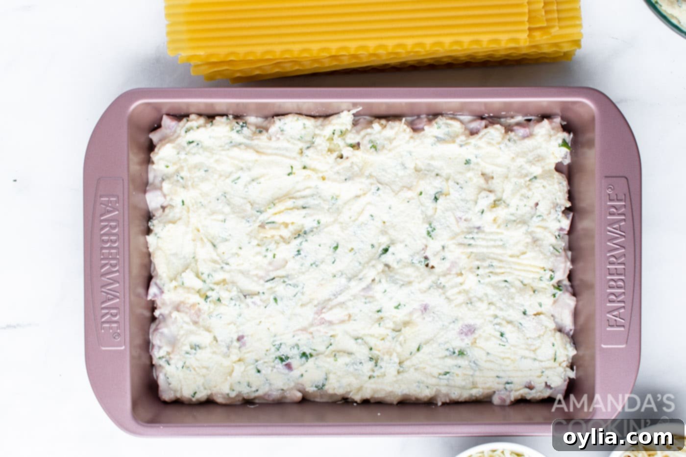 Spreading the ricotta mixture over a layer of ham and noodles in the baking pan.