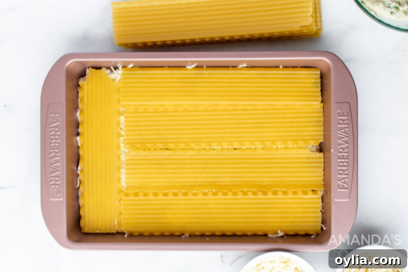 Adding the final layer of ham and ricotta over the noodles in the baking pan.