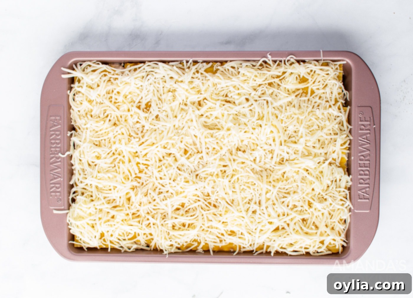 Topping the lasagna with the final layer of shredded Swiss and mozzarella cheese before baking.