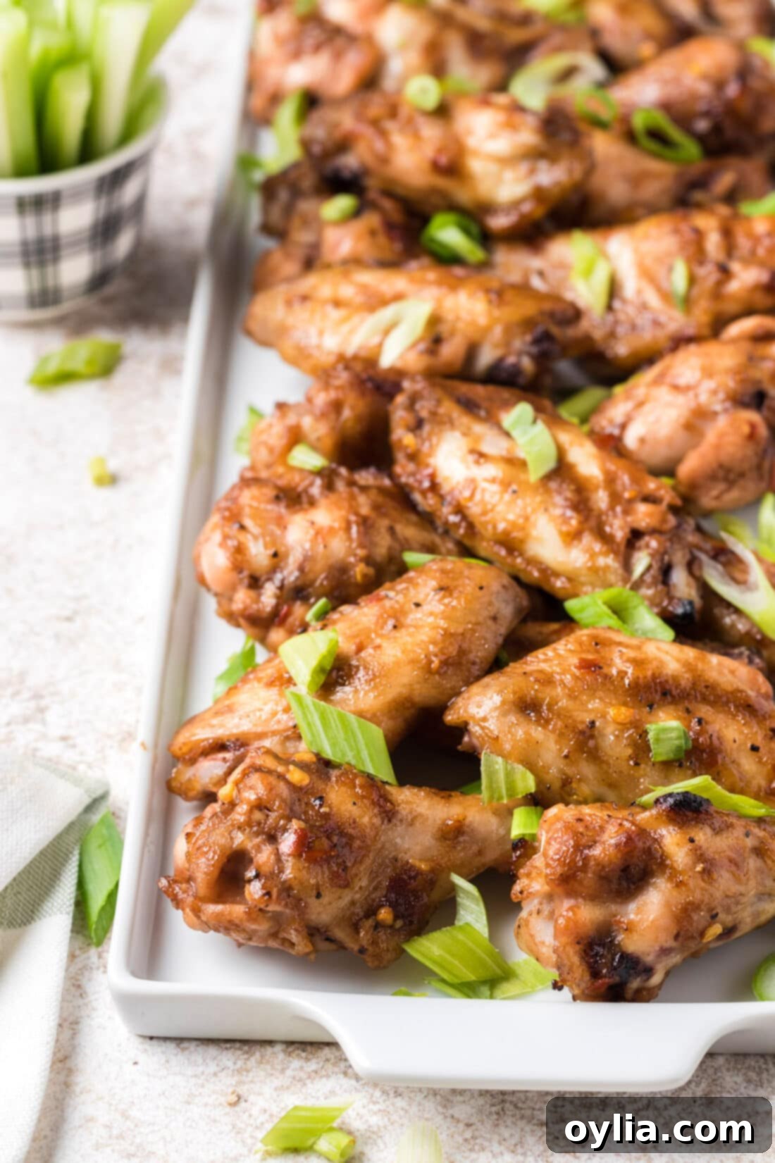 Plate piled high with delicious spicy sticky chicken wings, garnished with fresh green onions, ready to serve.