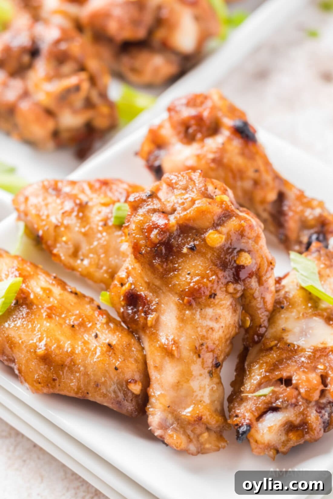 Close-up of a single spicy chicken wing on a white plate, showing its sticky glaze and a sprinkle of green onion.