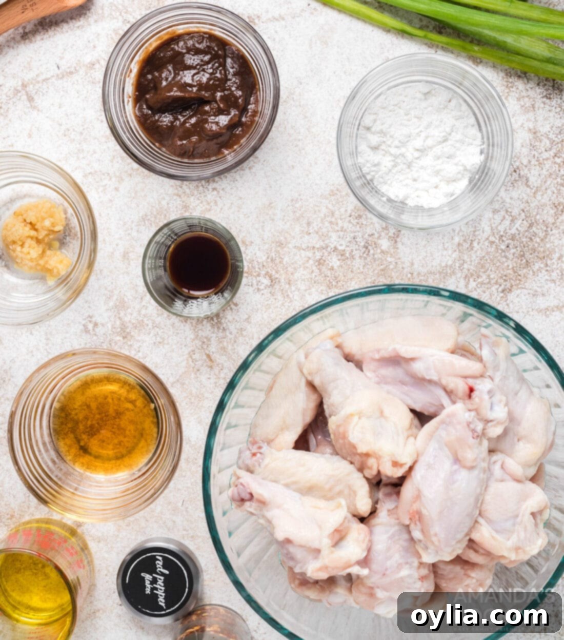 Various ingredients for making spicy sticky chicken wings laid out on a wooden cutting board.